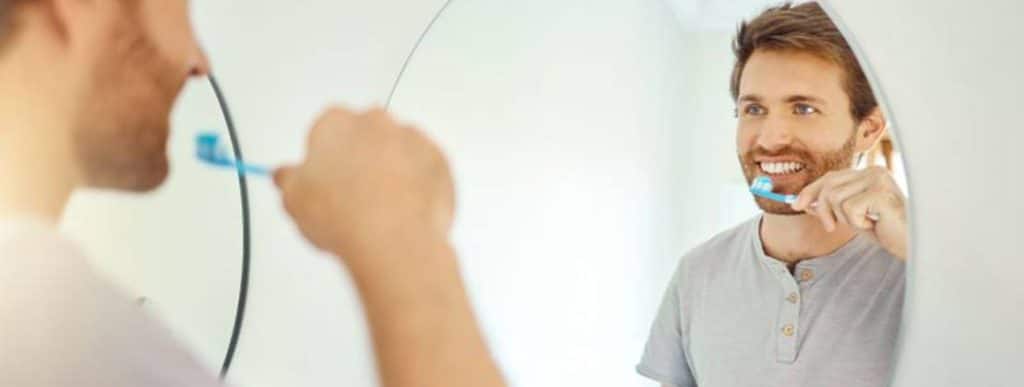 Man brushing his teeth in front of a bathroom mirror